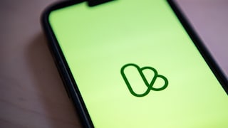 Nahaufnahme eines Smartphones mit grünem Bildschirm und dem Kleinanzeigen-Logo in der Mitte, der Hintergrund ist unscharf.