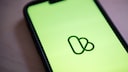 Nahaufnahme eines Smartphones mit gr&uuml;nem Bildschirm und dem Kleinanzeigen-Logo in der Mitte, der Hintergrund ist unscharf.