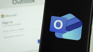 Outlook-Logo auf dem Smartphone, im Hintergrund Outlook-Anmeldefenster auf einem Computer