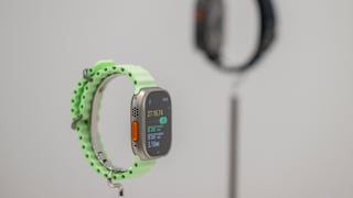 Apple Watch Ultra 3 mit hellgrünem Armband auf einem Ständer, im Hintergrund ist eine weitere Smartwatch unscharf zu sehen.