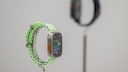 Apple Watch Ultra 3 mit hellgr&uuml;nem Armband auf einem St&auml;nder, im Hintergrund ist eine weitere Smartwatch unscharf zu sehen.