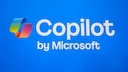 Alt-Text: Auf blauem Hintergrund ist das farbige Copilot-Logo neben dem wei&szlig;en Schriftzug &bdquo;Copilot&ldquo; zu sehen, darunter steht &bdquo;by Microsoft&ldquo;