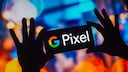 Zwei H&auml;nde halten ein Smartphone im Querformat vor einen unscharfen, bunt beleuchteten Hintergrund. Auf dem Display sind das farbige Google-Logo und der Schriftzug &bdquo;Pixel&ldquo; zu sehen. Im Hintergrund dominieren blaue, orangefarbene und violette Lichtfl&auml;chen und Bokeh-Effekte. Die H&auml;nde und das Smartphone erscheinen als dunkle Silhouetten vor den hellen Farben.