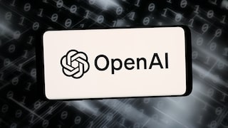 Ein Smartphone oder Display zeigt auf hellem Hintergrund das OpenAI-Logo und den Schriftzug „OpenAI“. Im Hintergrund sind unscharfe Reihen aus Nullen und Einsen sowie helle Lichtstreifen auf dunklem Grund zu sehen. Die Darstellung wirkt wie eine grafische Illustration zu den Themen Künstliche Intelligenz, Software und Cybersicherheit.