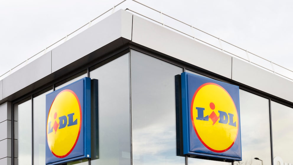 Außenansicht einer Lidl-Filiale mit zwei großen blau-gelben Lidl-Schildern an einer Glasfassade. Das Gebäude hat helle Fassadenelemente, große Fenster und ein flaches Dach mit Geländer.