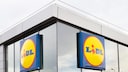 Au&szlig;enansicht einer Lidl-Filiale mit zwei gro&szlig;en blau-gelben Lidl-Schildern an einer Glasfassade. Das Geb&auml;ude hat helle Fassadenelemente, gro&szlig;e Fenster und ein flaches Dach mit Gel&auml;nder.