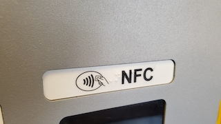 Nahaufnahme eines NFC-Symbols mit der Aufschrift „NFC“ an einem Kartenlesegerät oder Geldautomaten. Unterhalb des Symbols ist ein Teil des Displays zu sehen.