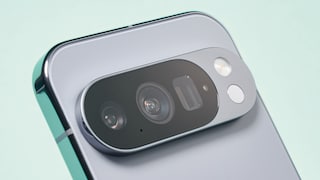 Nahaufnahme der Rückseite eines silberfarbenen Smartphones mit großem, ovalem Kameramodul. Sichtbar sind mehrere Kameralinsen, ein Blitz und weitere Sensoren in einer erhöhten Kameraleiste. Das Gerät ist schräg vor einem hellen, unscharfen Hintergrund fotografiert.