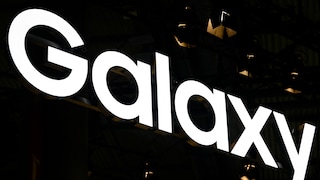 Leuchtender Samsung-Galaxy-Schriftzug vor dunklem Hintergrund. Zu sehen sind vor allem die großen weißen Buchstaben „Galaxy“, die schräg durch das Bild laufen. Im Hintergrund sind nur wenige dunkle Strukturen und kleine Lichtpunkte erkennbar.