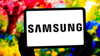 Ein Tablet wird mit beiden Händen vor einem unscharfen, bunten Hintergrund gehalten. Auf dem weißen Display ist mittig das schwarze Samsung-Logo zu sehen. Im Hintergrund sind kräftige Rot-, Gelb-, Grün- und Blautöne erkennbar.