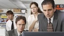 Die Figuren Dwight Schrute (Rainn Wilson), Michael Scott (Steve Carell), Pam Beesly (Jenna Fischer) und Jim Halpert (John Krasinski) blicken gemeinsam konzentriert auf einen Computerbildschirm.