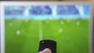 Person zeigt mit der Fernbedienung auf einen Fernseher
