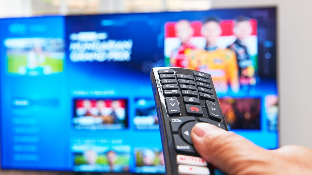 Person hält eine Fernbedienung auf einen Fernseher gerichtet