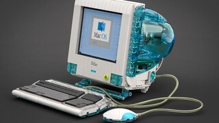 Lego-Nachbau eines Apple iMac G3 auf dunklem Hintergrund. Der Computer besitzt ein transparentes blaues Gehäuse mit integriertem Bildschirm, auf dem das Mac-OS-Logo zu sehen ist. Vor dem Rechner liegen eine passende Tastatur und die runde „Hockey-Puck“-Maus, die über transparente Kabel mit dem Modell verbunden sind.