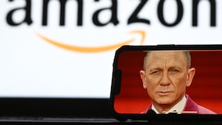 Smartphone mit dem Bild eines James-Bond-Darstellers auf dem Display. Im unscharfen Hintergrund ist das Amazon-Logo groß zu sehen. Das Foto illustriert Amazons Beteiligung an der Zukunft des James-Bond-Franchise.
