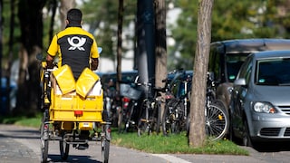 Ein Briefträger fäht mit seinem Fahrrad eine Straße in München entlang