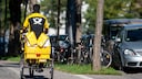 Ein Brieftr&auml;ger f&auml;ht mit seinem Fahrrad eine Stra&szlig;e in M&uuml;nchen entlang