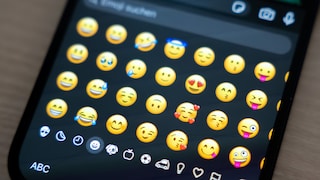 Nahaufnahme eines Smartphones mit weißem Bildschirm. In der Mitte ist das Logo der Google-Tastatur Gboard zu sehen: eine blaue Tastatur mit dem bunten Google-G auf einem weißen Symbol darüber. Am oberen Displayrand befindet sich eine kreisförmige Frontkamera. Das Gerät liegt schräg vor einem dunklen Hintergrund mit unscharfen blauen Tastaturtasten und einem roten Bereich links unten.
