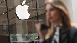 Apple-Logo über Store-Eingang, im Vordergrund Frau mit Smartphone