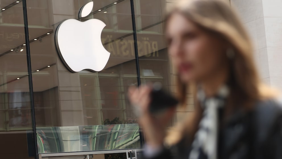 Apple-Logo über Store-Eingang, im Vordergrund Frau mit Smartphone