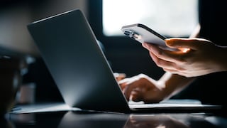 iPhone in der Hand, neben Laptop
