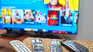 Mehrere Fernbedienungen liegen auf einem Tisch vor einem Fernseher