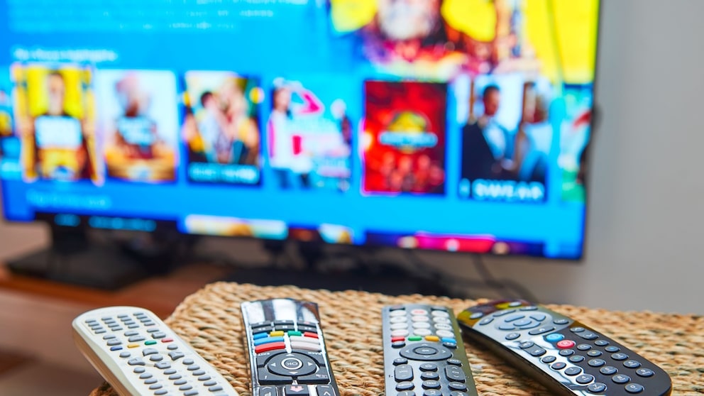 Mehrere Fernbedienungen liegen auf einem Tisch vor einem Fernseher