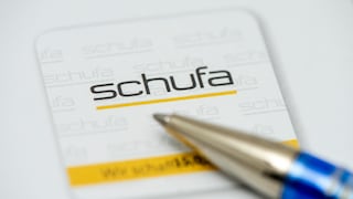Nahaufnahme eines Schufa-Dokuments mit dem Schufa-Logo in Schwarz und Gelb. Im Vordergrund liegt die Spitze eines blauen Kugelschreibers unscharf über dem Papier.