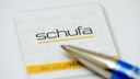 Nahaufnahme eines Schufa-Dokuments mit dem Schufa-Logo in Schwarz und Gelb. Im Vordergrund liegt die Spitze eines blauen Kugelschreibers unscharf &uuml;ber dem Papier.