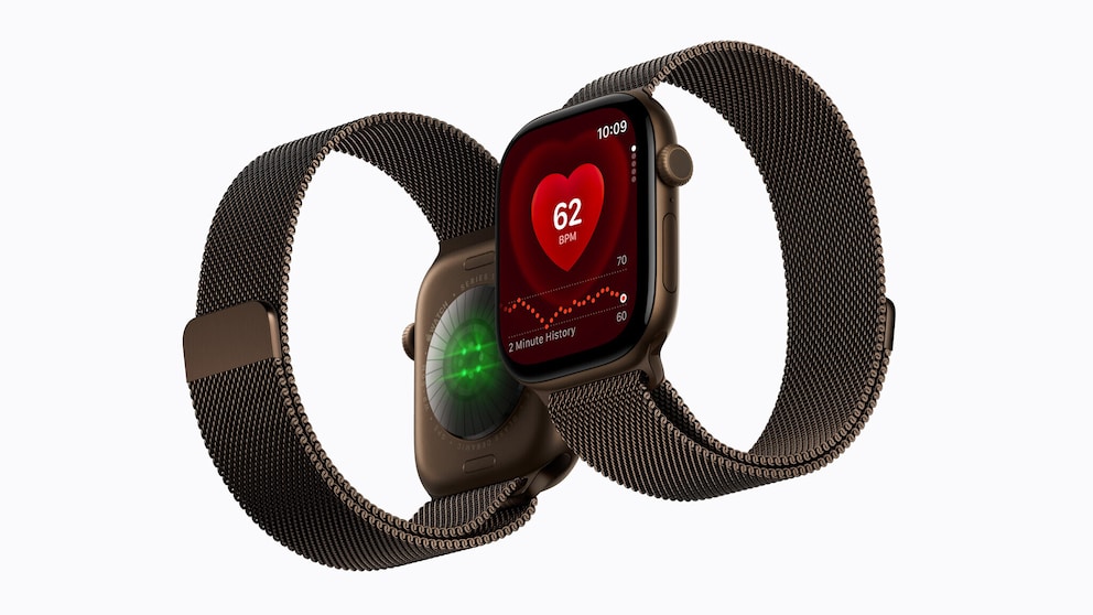 A brown Apple Watch with a brown metal band against a light background. The display shows a heart rate measurement with a value of 62 BPM. Behind the watch, the back of the case with green glowing sensors is visible.