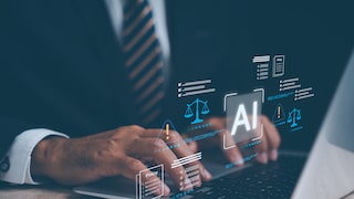 Ein Mann in Anzug sitzt an einem Schreibtisch und arbeitet mithilfe von AI auf seinem Laptop.