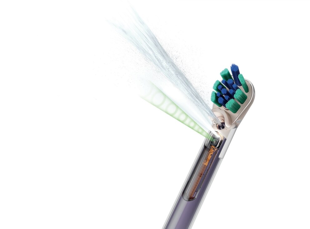 Close-up of a Dyson toothbrush with a partially transparent brush head. A water jet emerges from the head. Technical components are visible inside. The bristles are blue and green. The background is white.
