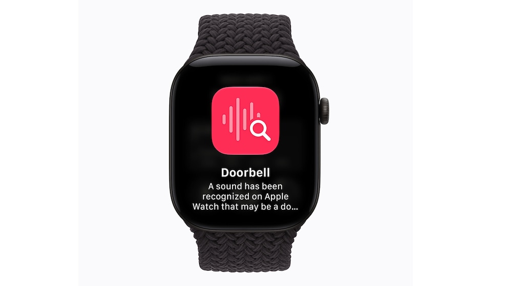 An Apple Watch with a dark blue braided band against a light background. The display shows a notification identifying a recognized sound as a doorbell. Above is a symbol for sound recognition.