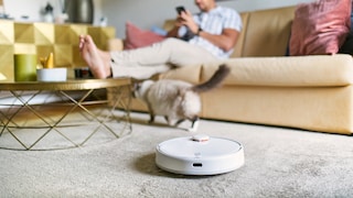 Man chilling at home on the sofa while robot vacuum cleaner is working