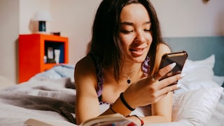 Frau liegt auf dem Bett und schaut auf ihr Smartphone