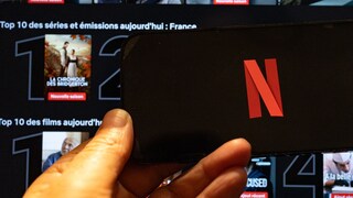 Netflix-Logo auf einem Smartphone, dahinter Streaming-Kacheln bei Netflix