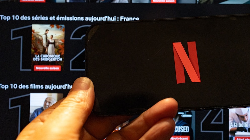 Netflix-Logo auf einem Smartphone, dahinter Streaming-Kacheln bei Netflix