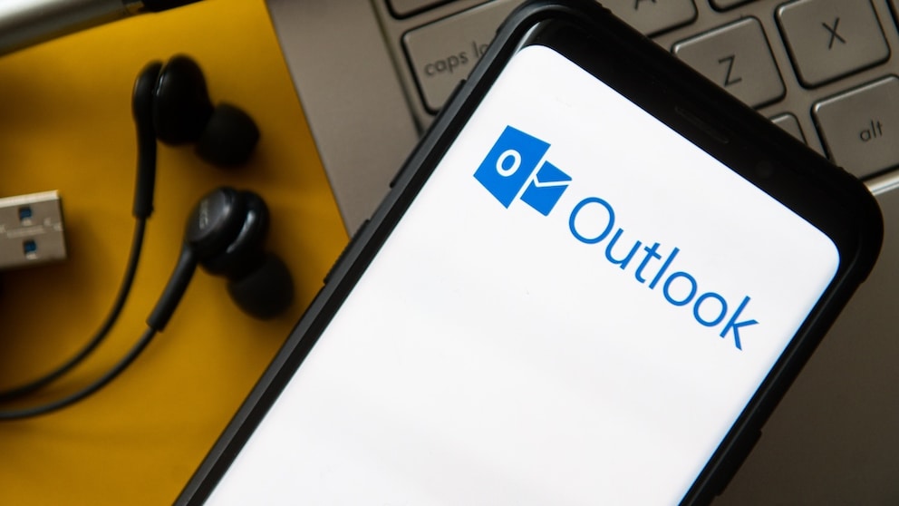 Outlook-Logo auf einem Smartphone, dazu Tastatur und Kopfhörer