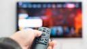 Person zeigt mit der Fernbedienung auf einen Fernseher