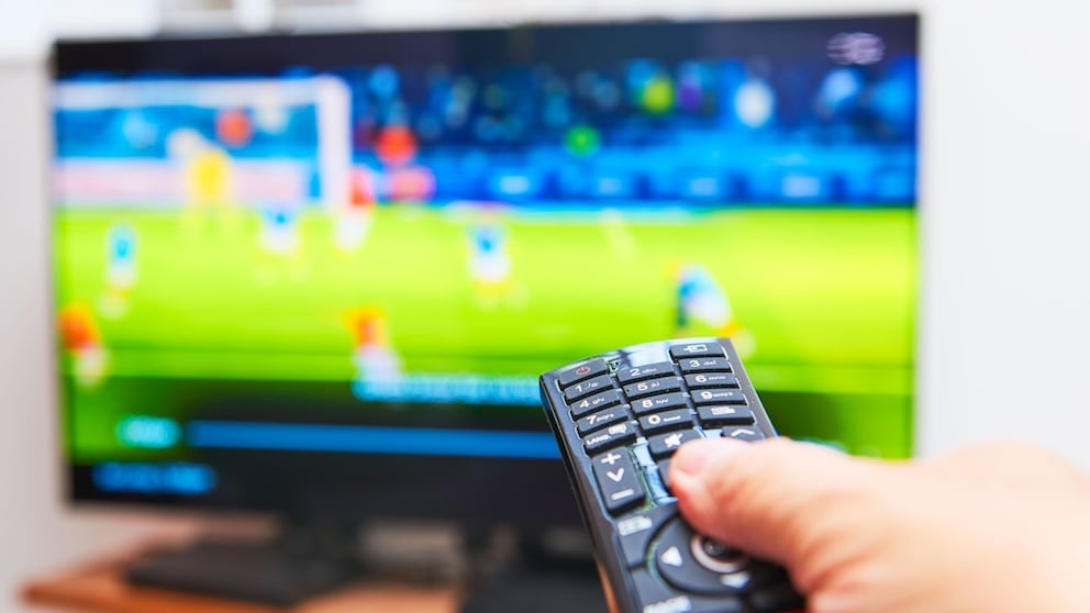 Person zeigt mit der Fernbedienung auf einen TV