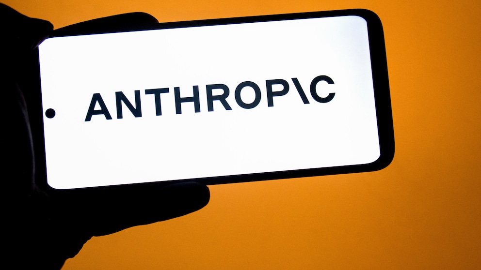 Ein Smartphone im Querformat zeigt das Logo von Anthropic auf einem hellen Display. Das Gerät wird vor einem orangefarbenen Hintergrund gehalten.