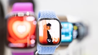 Eine Apple Watch mit hellblauem Armband steht im Vordergrund. Auf dem Display ist ein Zifferblatt mit einer Person im Profil zu sehen. Im unscharfen Hintergrund befinden sich weitere Apple Watches mit unterschiedlichen Armbändern und farbigen Anzeigen.