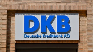 Blaues DKB-Logo mit der Aufschrift „Deutsche Kreditbank AG“ auf einem weißen Schild an einer Backsteinfassade über einem Eingangsbereich.
