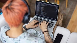 Ein junger Mann mit roten Haaren sitzt in einem modernen Warteraum auf einem Sessel. Auf seinem Schoß liegt ein Laptop, auf dessen Tastatur er gerade tippt. Er trägt Kopfhörer und ist ganz auf den Bildschirm konzentriert.