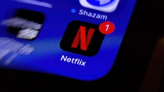 Nahaufnahme eines Smartphone-Bildschirms mit dem Netflix-App-Symbol. Das rote Netflix-Logo auf schwarzem Hintergrund ist mittig zu sehen und trägt ein rotes Benachrichtigungsfeld mit der Zahl 1. Darüber befindet sich das App-Symbol von Shazam auf blauem Hintergrund. Der Bildschirm ist unscharf dargestellt und zeigt einen starken Zoom-Effekt.