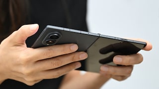 Eine Person hält ein aufgeklapptes Samsung Galaxy Z Fold 8 mit beiden Händen. Zu sehen sind die Rückseite mit Kameramodul sowie das Scharnier des faltbaren Smartphones. Der Hintergrund ist unscharf.