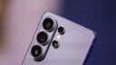 Nahaufnahme der R&uuml;ckseite eines silberfarbenen Samsung-Smartphones mit mehreren Kameralinsen vor unscharfem blau-violettem Hintergrund