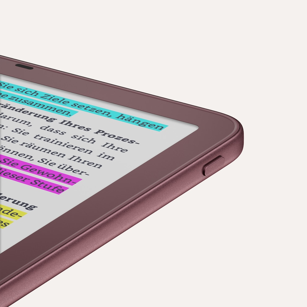Close-up of a violet Amazon Kindle e-reader against a light background. Visible are the top right corner of the device, a side button, and part of the E-Ink display. The screen shows German text highlighted in several places with blue, pink, and yellow markings. The casing has a matte, slightly glossy surface.