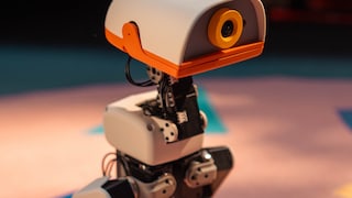 Nahaufnahme des Roboters MicroDuck mit weißem Gehäuse, orangefarbenen Details und einer Kamera im Kopf. Mechanische Gelenke und Kabel sind sichtbar.