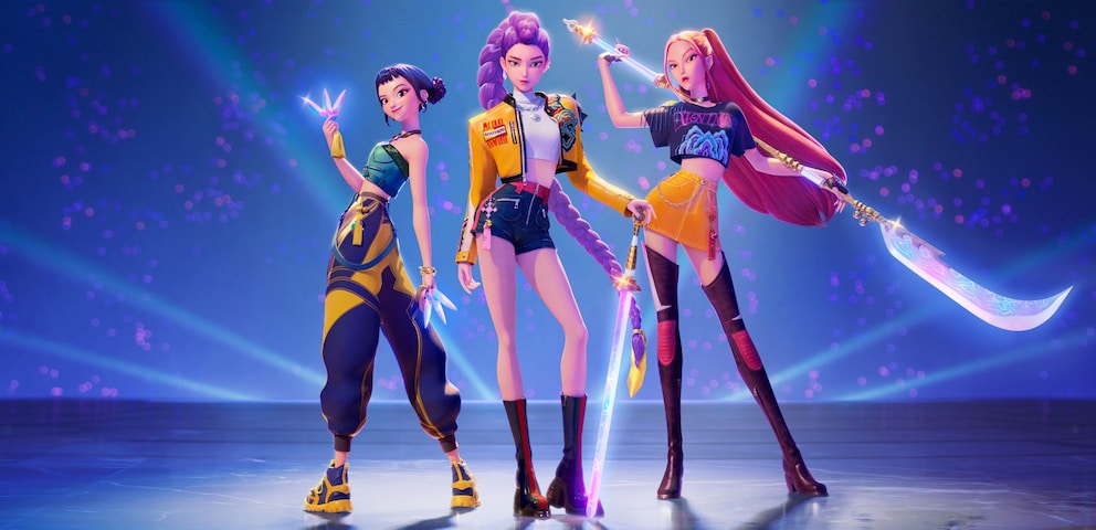 Three animated figures stand side by side on a lit stage against a blue-violet background with numerous light points. The figure on the left holds a glowing, crystal-like object and wears a blue-yellow outfit. The middle figure has long violet hair, a yellow jacket, and holds a glowing sword. The figure on the right wears a dark top, an orange skirt, and high boots, holding a large, curved weapon over the shoulder. Several light effects and colored beams are visible in the background.